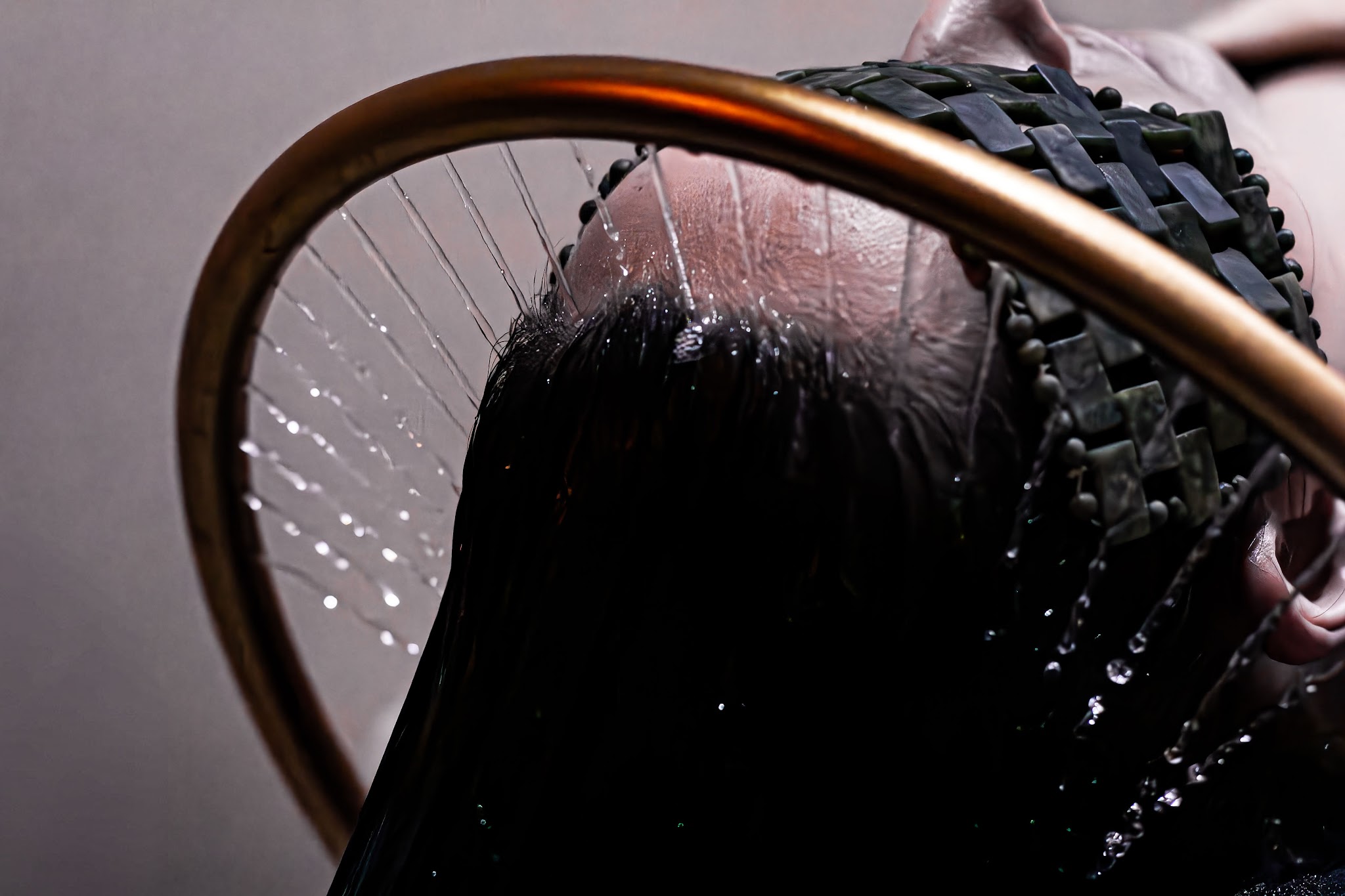 The halo waterfall rinse: fine streams of water falling from a gold halo over a client's hair, with a woven jade eye mask