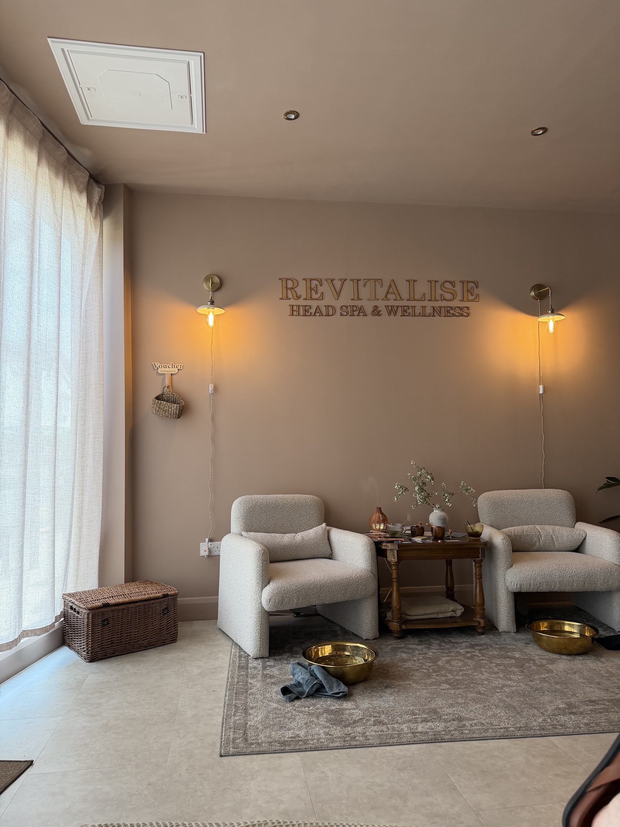 The Revitalise reception lounge: two cream armchairs, gold foot bowls and the REVITALISE Head Spa & Wellness lettering on the wall