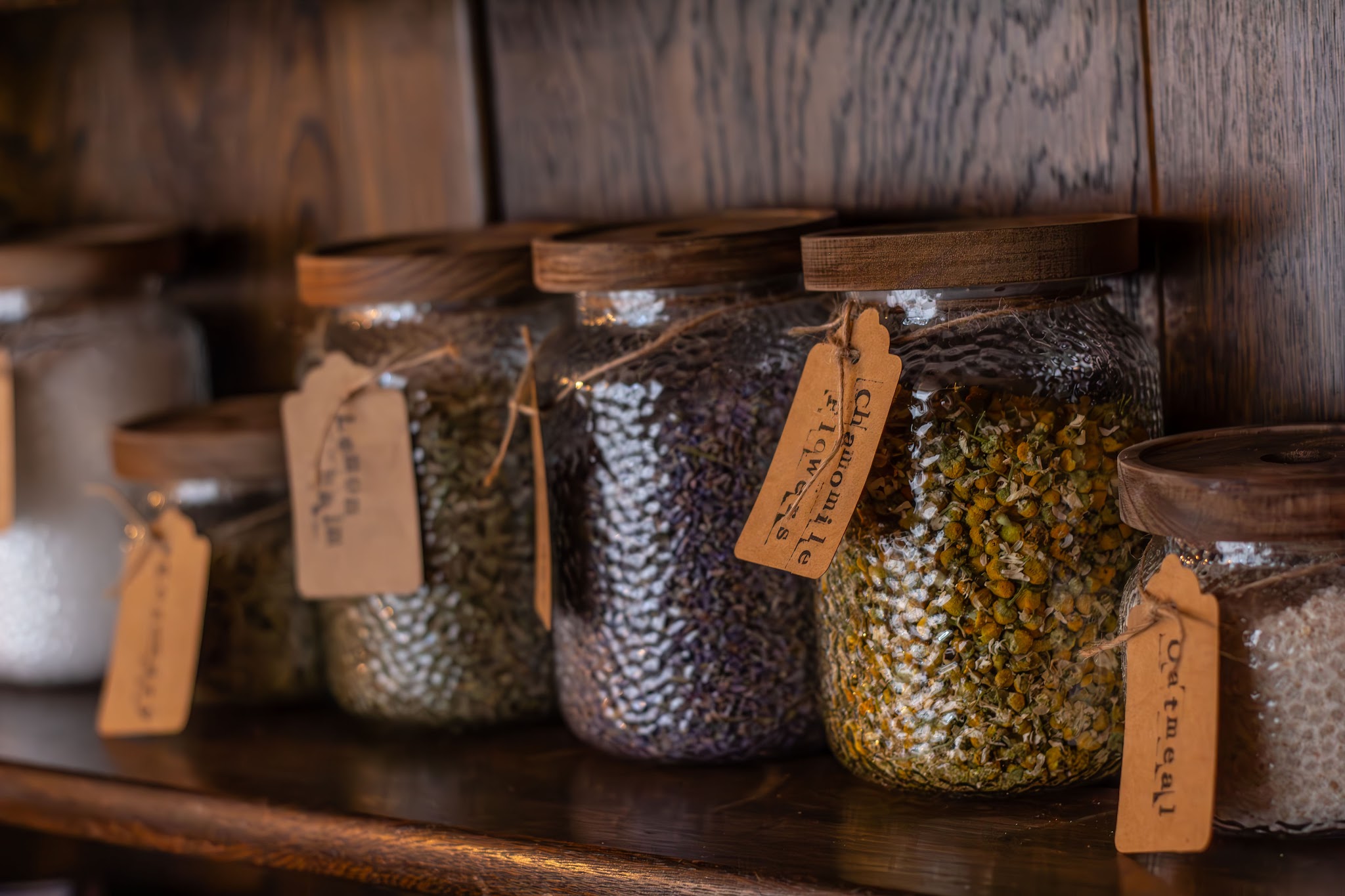 Glass jars of dried botanicals and mineral salts with handwritten kraft tags at the foot soak bar